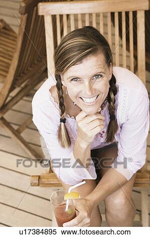Portrait of a mid adult woman sitting on a chair and holding a glass of cocktail View Large Photo Image Stock Photography - Portrait of a mid adult woman sitting on a chair and holding a glass of cocktail. Fotosearch