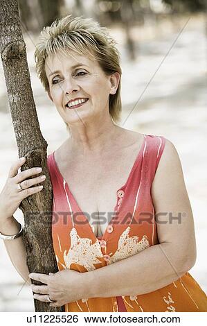Close-up of a mature woman leaning against a tree trunk and smiling View Large Photo Image Stock Photograph - Close-up of a mature woman leaning against a tree trunk and smiling. Fotosearch