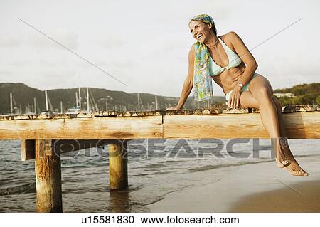 Stock Image - Mid adult woman sitting on a pier and smiling. Fotosearch