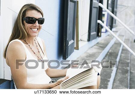 Mid adult woman sitting on steps and holding a book View Large Photo Image Stock Image - Mid adult woman sitting on steps and holding a book. Fotosearch
