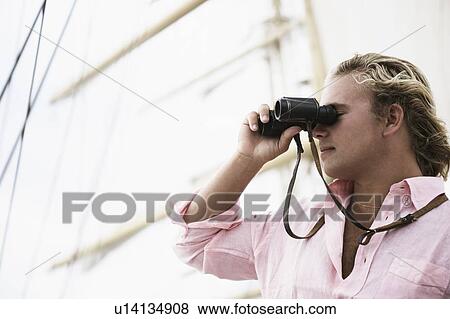 Close-up of a young man looking through binoculars View Large Photo Image Stock Photo - Close-up of a young man looking through binoculars. Fotosearch
