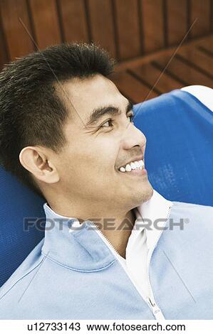 High angle view of a young man reclining on a lounge chair and smiling View Large Photo Image Stock Image - High angle view of a young man reclining on a lounge chair and smiling. Fotosearch
