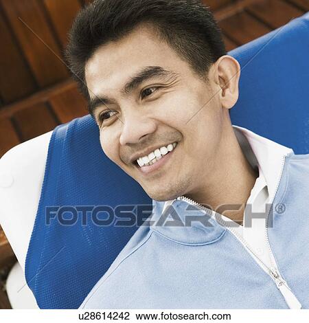 High angle view of a young man reclining on a lounge chair and smiling View Large Photo Image Stock Image - High angle view of a young man reclining on a lounge chair and smiling. Fotosearch