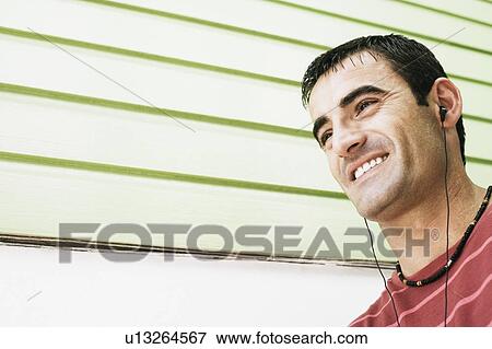 Low angle view of a mid adult man listening to earbuds and smiling View Large Photo Image Stock Photo - Low angle view of a mid adult man listening to earbuds and smiling. Fotosearch