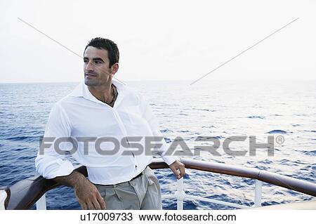 Mid adult man leaning against the railing of a ship View Large Photo Image Stock Image - Mid adult man leaning against the railing of a ship. Fotosearch