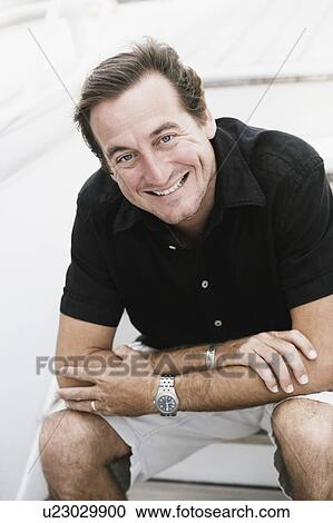 Stock Image - Portrait of a mid adult man sitting on a staircase and smiling. Fotosearch