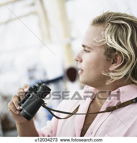 Side profile of a young man holding a pair of binoculars View Large Photo Image Stock Image - Side profile of a young man holding a pair of binoculars. Fotosearch