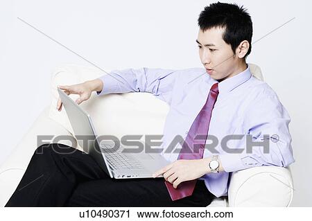 Close-up of a businessman sitting in an armchair and using a laptop View Large Photo Image Stock Image - Close-up of a businessman sitting in an armchair and using a laptop. Fotosearch