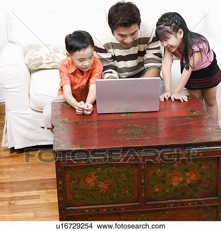 Mid adult man using a laptop with his son and daughter beside him View Large Photo Image Picture - Mid adult man using a laptop with his son and daughter beside him. Fotosearch