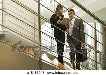 Stock Photo - Businessman and businesswoman on staircase discussing over document. Fotosearch