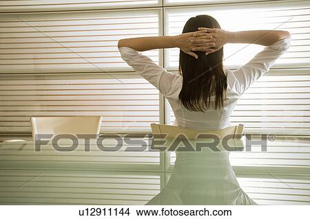 Back view of businesswoman in office with hands behind head View Large Photo Image Picture - Back view of businesswoman in office with hands behind head. Fotosearch