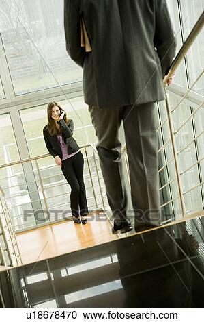 Businesswoman on cell phone and businessman walking down staircase View Large Photo Image Stock Image - Businesswoman on cell phone and businessman walking down staircase. Fotosearch