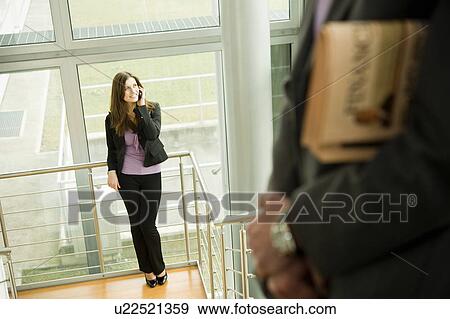 Businesswoman on cell phone and businessman with financial newspaper on staircase View Large Photo Image Stock Photo - Businesswoman on cell phone and businessman with financial newspaper on staircase. Fotosearch