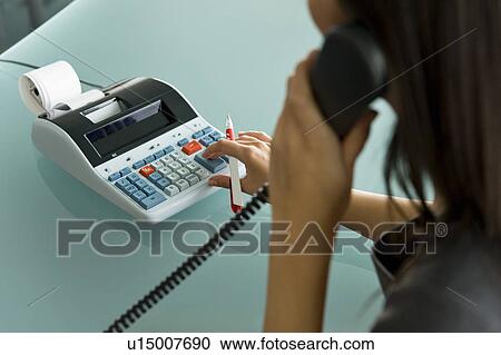 Stock Image - Professional woman on telephone using calculator. Fotosearch