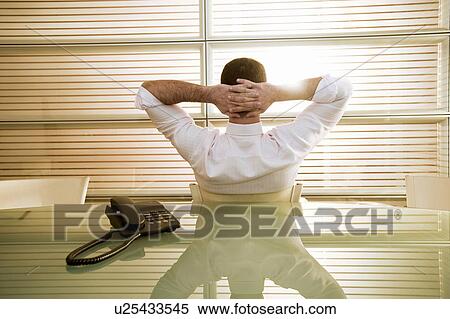 Stock Photography - Back view of businessman in office with hands behind head. Fotosearch