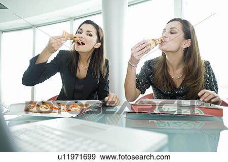 Stock Photo - Businesswomen eating pizza at desk. Fotosearch