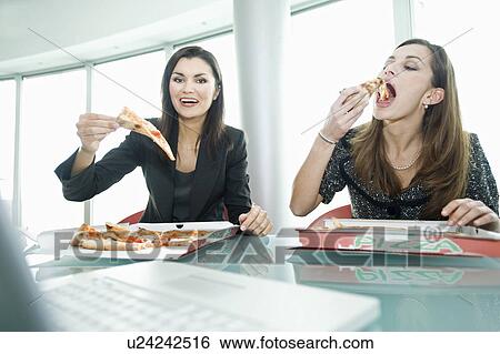 Businesswomen eating pizza at desk View Large Photo Image Stock Photograph - Businesswomen eating pizza at desk. Fotosearch