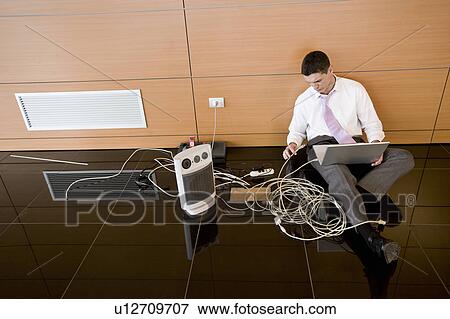 Stock Photo - Office worker on floor with wires and laptop. Fotosearch