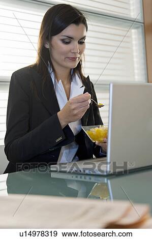 Professional woman eating fruit salad over laptop View Large Photo Image Stock Photo - Professional woman eating fruit salad over laptop. Fotosearch