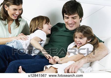 Stock Photo - Young couple on couch with children laughing. Fotosearch