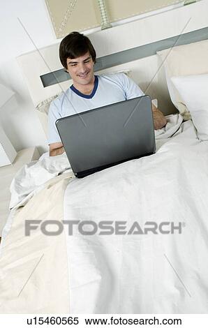 Young man in bed with laptop computer View Large Photo Image Stock Photography - Young man in bed with laptop computer. Fotosearch