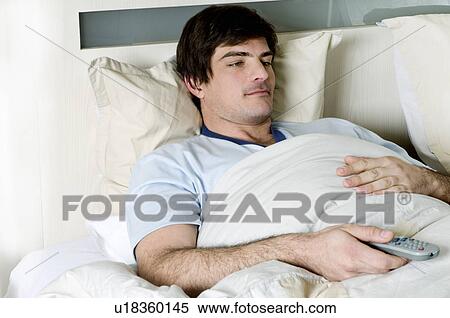 Stock Photography - Young man in bed with remote control. Fotosearch