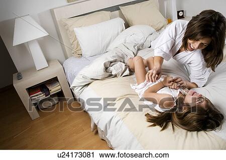 Stock Image - Young woman and girl on bed laughing. Fotosearch