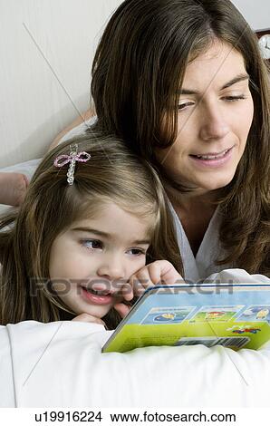 Young woman and girl on bed reading a book View Large Photo Image Picture - Young woman and girl on bed reading a book. Fotosearch