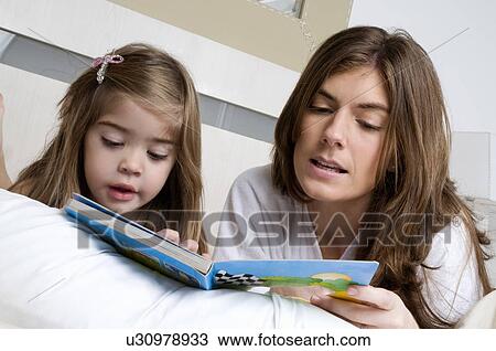 Stock Image - Young woman and girl on bed reading a book. Fotosearch