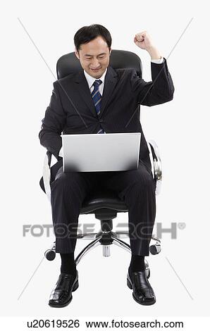 Stock Photograph - Businessman sitting on chair and using laptop with one fist up, Business People. Fotosearch