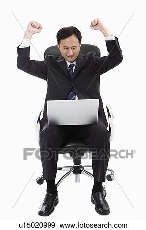 Stock Photo - Businessman sitting on chair, looking at laptop with fists up, Business People. Fotosearch