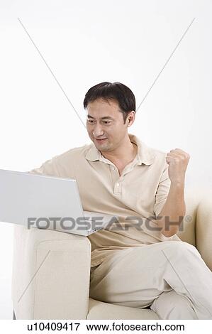 Businessman sitting on sofa and using laptop with fists up, Business People View Large Photo Image Stock Photo - Businessman sitting on sofa and using laptop with fists up, Business People. Fotosearch