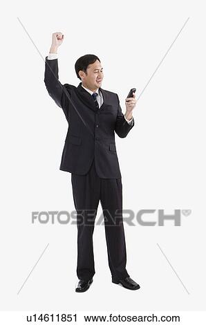 Stock Image - Businessman using mobile phone with fists up, Business People. Fotosearch