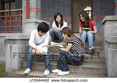 Stock Image - Four college students reading books on the stairs, Studying, Education. Fotosearch