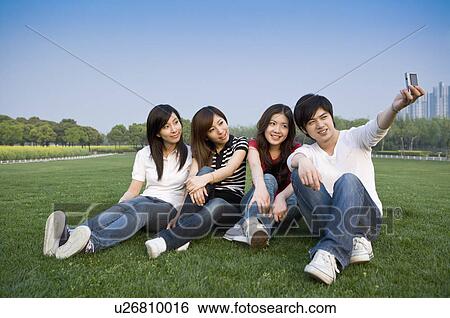 Stock Photograph - Four people sitting on lawn and taking pictures. Fotosearch