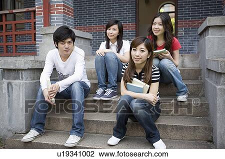 Stock Image - Four young college students sitting on the stairs and studying together, Studying, Education. Fotosearch