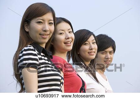 Stock Photo - Four young people standing in a row and smiling happily. Fotosearch