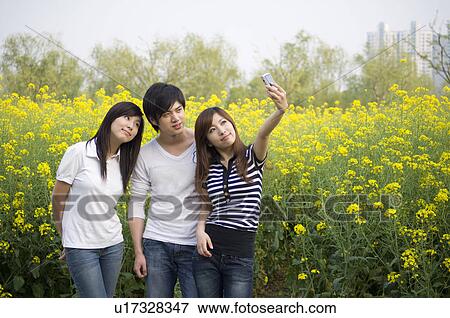 Stock Photo - Three young people taking pictures near the flower field. Fotosearch