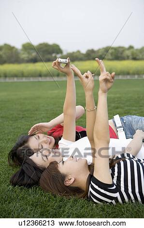 Three young women lying on the lawn and taking pictures View Large Photo Image Stock Image - Three young women lying on the lawn and taking pictures. Fotosearch