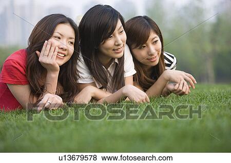 Stock Photo - Three young women lying on the lawn together, Studying, Education. Fotosearch