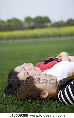 Stock Photo - Three young women lying on the lawn. Fotosearch
