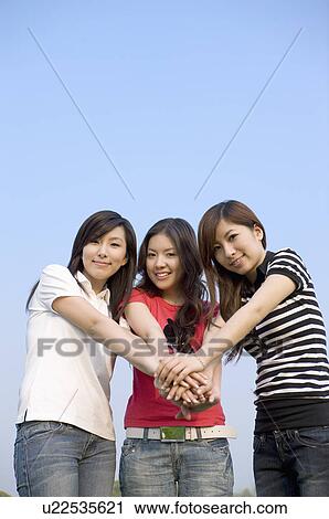 Stock Image - Three young women putting hands of a stack, Studying, Education. Fotosearch