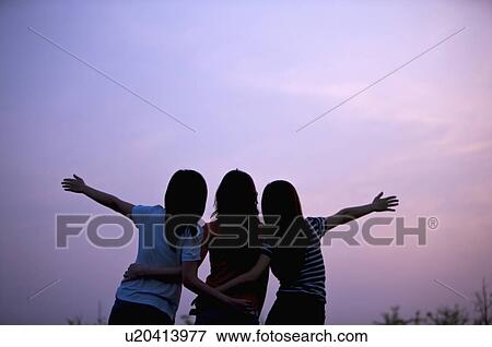 Three young women standing together with arms outstretched View Large Photo Image Stock Photo - Three young women standing together with arms outstretched. Fotosearch