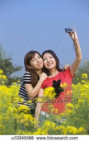 Two young women taking pictures in the flower field View Large Photo Image Stock Photo - Two young women taking pictures in the flower field. Fotosearch