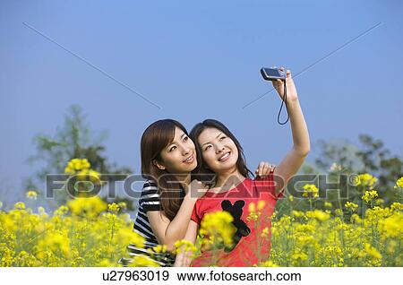 Stock Photo - Two young women taking pictures in the flower field. Fotosearch