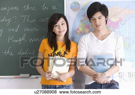 Stock Photo - Young man and woman holding books and standing in the classroom, Studying, Education. Fotosearch