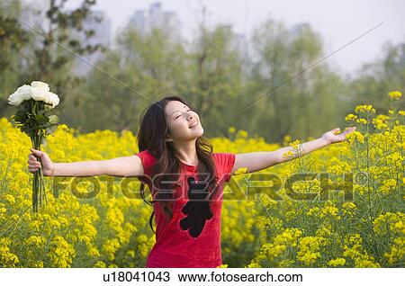 Stock Image - Young woman holding a bunch of flowers and standing in the flower field. Fotosearch