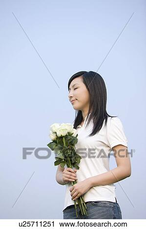 Stock Image - Young woman holding a bunch of flowers and closing her eyes. Fotosearch