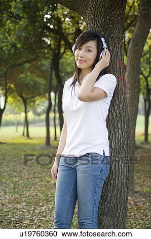 Stock Image - Young woman leaning on a tree and listening music. Fotosearch