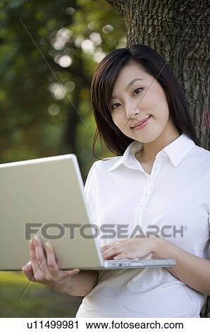 Young woman leaning on tree and using laptop, Studying, Education View Large Photo Image Stock Image - Young woman leaning on tree and using laptop, Studying, Education. Fotosearch